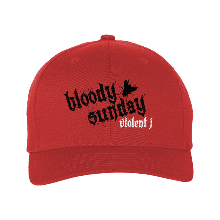 image of the front of a red flexfit hat on a white background. hat has a black print in the center that says bloody sunday. white below says violent j. 